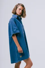 Vestido corto de denim azul oscuro, con cuello camisero, mangas cortas, cierre frontal con botones, bolsillo aplicado en el pecho y calce holgado.