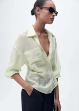 Camisa color verde agua, de corte cruzado con lazo en la cintura, cuello camisero, manga larga y bolsillo de parche en el pecho.