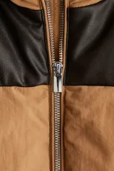 Chaleco puffer acolchado con diseño de bloques de color, combinando cuerpo en tono tostado con canesú en contraste de material revestido oscuro. Presenta cuello elevado, cierre frontal completo y bolsillos laterales insertados.