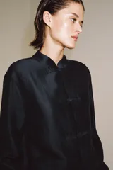 Camisa de estilo oriental confeccionada en mezcla de lyocell con acabado satinado. Presenta cuello redondo, manga larga con puños rectos, bolsillos de plastrón y cierre frontal mediante alamares.