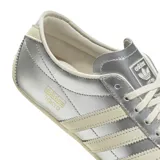 Championes Adidas modelo Tokyo, con diseño de perfil bajo en color plateado metalizado. Presenta las icónicas tres tiras laterales y suela en tono crema, con el logo de la marca y el nombre del modelo grabados en el lateral.