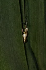 Blusa de manga larga color verde oliva, confeccionada en tejido satinado con textura acanalada. Presenta escote redondo con lazo ajustable que termina en un dije dorado, y el bajo es abullonado con elástico interior.