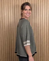 Buzo de punto negro con diseño holgado, mangas codo y detalles en tono tostado y blanco en el cuello redondo, puños y ruedo.