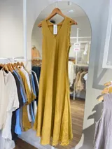 Vestido largo sin mangas, color beige claro, con escote en V y textura arrugada o arrugada, con terminación deshilachada en el ruedo.