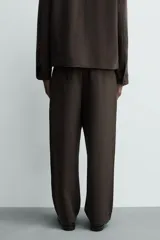 Pantalón de corte relajado con pliegues frontales, bolsillos laterales y bolsillos traseros de vivo. Presenta cierre frontal con cremallera y botón.