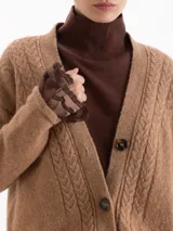 Cardigan de tejido de punto color marrón, con diseño de trenzas verticales, escote en V y cierre frontal con botones oscuros. Presenta mangas largas con puños acanalados y un corte holgado.