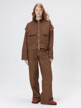 Pantalón de tiro medio y pierna ancha confeccionado en denim de algodón grueso. Presenta un diseño a rayas verticales en tonos azul y celeste, con costuras en contraste color rojo, bolsillos laterales tipo cargo y remaches metálicos.