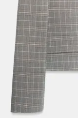 Blazer corta de corte recto con estampado de cuadros, cuello con solapas de muesca, hombreras y manga larga. Presenta un diseño cruzado con doble botonadura y falsos bolsillos con solapa en el frente.