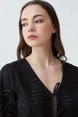 Blusa negra de broderie con escote en V y lazos para atar en el frente. Tiene mangas cortas con terminación de puntilla. 