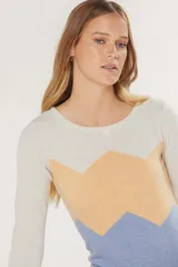 Buzo de tejido de punto fino con diseño de bloques de color en forma de zigzag en tonos lila y amarillo sobre base color crema. Presenta cuello redondo y mangas largas.