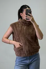 Chaleco de piel sintética color beige, con cuello alto, cierre frontal y bolsillos laterales.