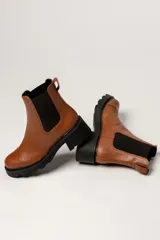 Bota tipo Chelsea de cuero color verde oliva, con paneles laterales elásticos negros y suela track de goma negra con taco cuadrado.