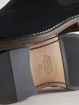 Bota Chelsea de gamuza gris con elásticos laterales, suela de goma marrón y tirador trasero.