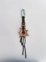 Charm para bolso o accesorios con mosquetón metálico, tejido de macramé en cordón negro y dijes de cerámica esmaltada en tonos violeta y celeste.