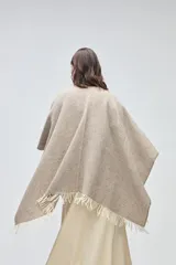 Ruana de lana sin teñir en tono marrón jaspeado, con diseño envolvente y terminaciones de flecos en color crudo.
