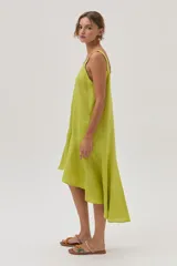Vestido de lino color lima, corto al frente y más largo en la espalda, con volado en el bajo que aporta movimiento y frescura.