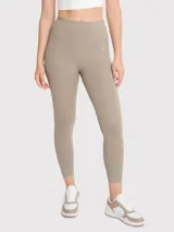 Calza deportiva de tiro alto con largo hasta el tobillo, confeccionada en tejido elástico de color beige. Presenta un diseño minimalista sin bolsillos y cuenta con un pequeño logo reflectante en la cadera.