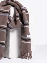 Bufanda de tejido suave en color marrón chocolate con diseño de rayas horizontales en tonos naranja, beige y gris. Presenta terminaciones con flecos en los extremos.