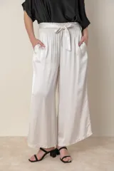 Pantalón palazzo color blanco hueso, de tela satinada, con cintura elastizada, lazo de ajuste y bolsillos laterales.