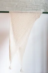 Chal triangular tejido a mano en lana de alpaca natural color crudo, con diseño calado y terminación con borlas.