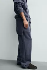 Pantalón jogger de corte wide fit confeccionado en algodón con interior de rizo. Presenta cintura elástica ajustable con cordón, bolsillos laterales y un bolsillo trasero de plastrón. Cuenta con un efecto lavado y acabados irregulares en el ruedo.