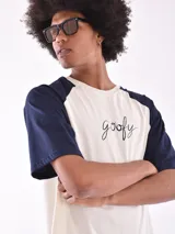 Remera de mangas cortas ranglan, color crudo con mangas azul marino y estampado frontal con la palabra "goofy" en cursiva.