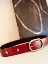 Cinturón de cuero color borgoña con apliques de estrellas doradas y hebilla metálica envejecida.
