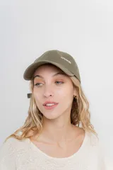 Gorra verde militar de diseño clásico con visera curva y aplique metálico plateado con la inscripción "Peach" en el lateral frontal. Cuenta con tira ajustable en la parte trasera.