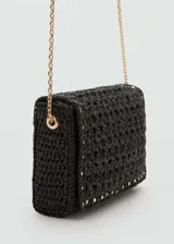 Bolso tipo sobre de fibra natural tejida en color negro, con detalle de tachuelas metálicas doradas en el borde. Cuenta con cierre de solapa con botón magnético, forro interior y asa larga de cadena metálica dorada.
