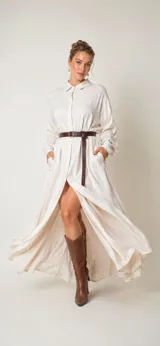 Vestido largo tipo camisero de satén, color marfil, con cuello camisero, cierre frontal de botones, mangas largas con puños y bolsillos laterales. Diseño holgado con caída fluida.