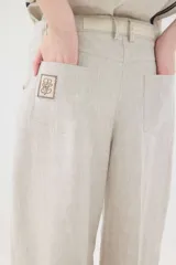 Pantalón de lino marrón de tiro medio, con calce holgado y diseño de piernas amplias. Cuenta con bolsillos traseros, trabillas para cinto y un pin bordado en contraste.