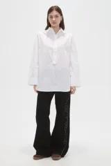 Camisa de algodón blanca de corte holgado, con cuello clásico, cierre frontal parcial con botones y mangas largas con puños anchos.