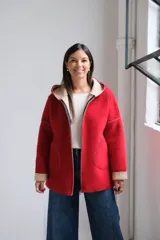 Tapado de paño rojo con capucha, cierre frontal y detalles en color beige en el interior, puños y bordes de los bolsillos. Presenta un corte recto y holgado.