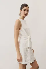 Vestido corto blanco sin mangas, con cuello redondo y detalle de nudo drapeado en el lateral.