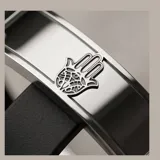 Pulsera de diseño masculino con placa central de acero inoxidable que presenta un grabado de una mano de Hamsa. La estructura se complementa con una banda de goma negra, ofreciendo un estilo moderno y resistente.