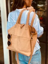 Bolso tipo tote de cuero sintético color beige con textura tipo cocodrilo. Tiene doble asa de mano y correa larga extraíble y ajustable. Cuenta con cierre principal, dos bolsillos externos y un bolsillo interno con cierre.