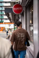 Remera oversize marrón de algodón elastizado con estampado en la espalda que incluye el texto "Crazy Hermod movement" y un diseño de zapatilla alada.
