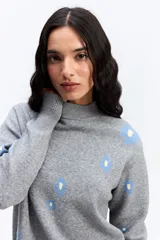 Sweater de tejido de punto color marrón con diseño estampado de flores en tonos rosados. Presenta cuello alto, mangas largas con puños ajustados y un corte relajado con terminación recta en la cintura.