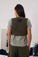 Chaleco de gabardina color blanco, con escote en V, cierre frontal con botones y bolsillos delanteros simulados.