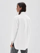 Camisa de corte oversize confeccionada en tela oxford de algodón. Presenta cuello clásico, cierre frontal con botones, mangas largas con puños y un bolsillo frontal con etiqueta de marca.