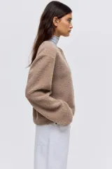 Chaqueta de sherpa suave con cuello redondo, corte holgado y cierre frontal con botones metálicos. Presenta ribetes de cinta en los bordes.