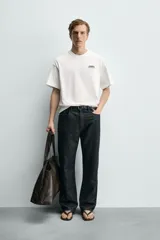 Camiseta de corte relajado, cuello redondo y manga corta. Presenta un pequeño estampado de texto en el pecho y un estampado gráfico de mayor tamaño en la espalda.