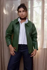 Campera de cuero color verde, con cierre frontal, cuello clásico y mangas largas. Presenta un diseño minimalista con un pequeño parche de cuero en el ruedo.