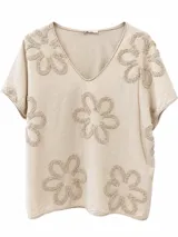 Remera beige de manga corta y cuello en V, con detalles de flores bordadas en relieve con textura.