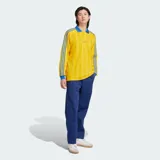 Camiseta de manga larga Adidas Originals, de corte holgado y color amarillo con rayas verticales sutiles en tono más oscuro y detalles en azul en cuello polo, puños y las clásicas franjas en las mangas. Cuenta con el logo bordado en el pecho.