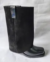 Bota de cuero negro con diseño 2 en 1, que incluye una polaina de gamuza desmontable. Presenta una base de bota de cuero liso y una caña alta de gamuza, ofreciendo versatilidad para diferentes estilos.
