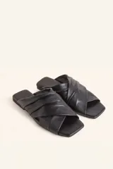 Sandalia tipo slide de cuero vacuno color blanco, con diseño de tiras cruzadas y fruncidas. Presenta una puntera cuadrada y una suela plana de cuero con un pequeño taco de 2 cm.
