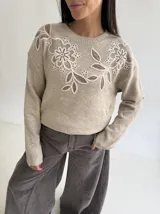 Sweater de punto color beige con cuello redondo, manga larga y detalle de bordado floral en la parte superior del pecho.