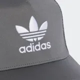 Gorra tipo trucker de cinco paneles en color gris, con paneles traseros y laterales de malla transpirable. Presenta el logo del Trifolio de Adidas bordado en blanco en la parte frontal, visera precurvada y cierre trasero ajustable a presión.