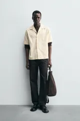 Camisa de corte relajado confeccionada en tejido de algodón, con cuello bowling y manga corta. Presenta un diseño con bordados geométricos a tono y cierre frontal de botones.